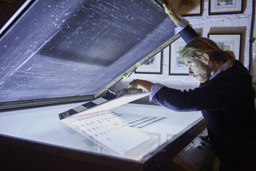 Young man preparing screen frame on lightbox in traditional print workshop