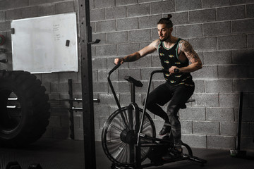 Fototapeta na wymiar young man using exercise bike at the gym. Fitness male using air bike for cardio workout at crossfit gym.