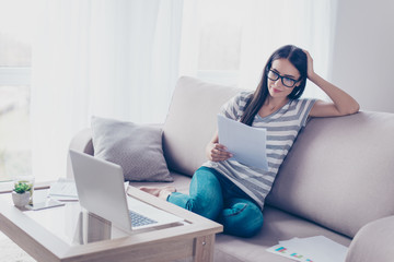 Smiling young pretty woman sitting on sofa working with computer and doing paperwork at home