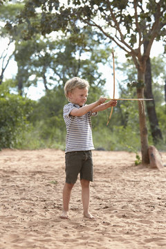 Young boy on sand holding home-made bow and arrow