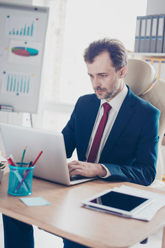 Close up portrait of busy realtor typing at his laptop in the modern office. He is wearing formalwear and concentrated at project