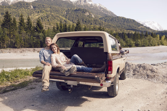 Couple sitting on back of pick up truck, looking at camera, Wallgau, Bavaria, Germany