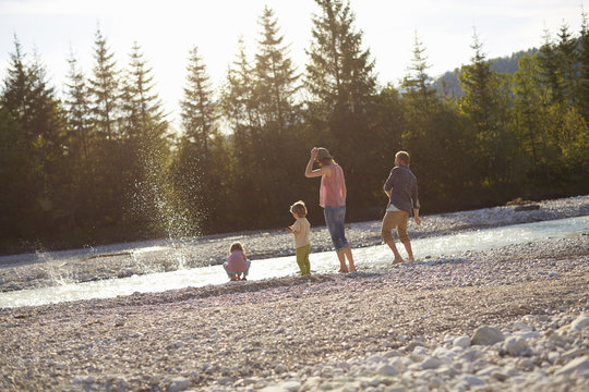 Rear view of family skimming stones on river