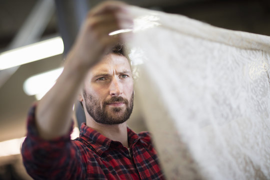 Male weaver checking lace textile in old textile mill