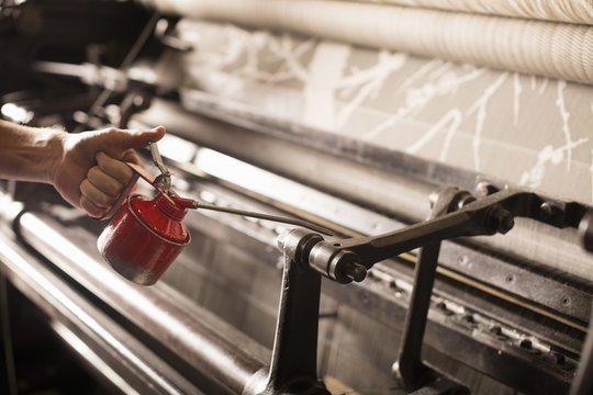 Hand of male weaver oiling old weaving machine in textile mill