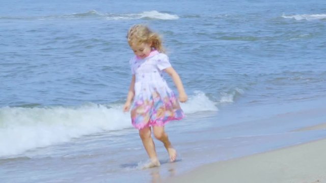 Adorable little girl  in a dress runs  jumping on the beach.  Child enjoys playing on the seashore running on the water with pleasure. splashing in sea waves.