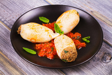 Squid stuffed with meat and vegetables, garnished with meant on black plate