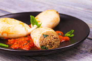 Squid stuffed with meat and vegetables, garnished with meant on black plate