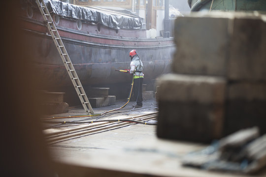 Worker sandblasting boat in shipyard