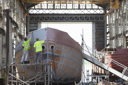 Two workers painting boat in shipyard
