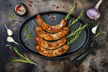 Grilled homemade rosemary sausages skewers on iron frying pan over rustic dark stone kitchen table. Top view, flat lay