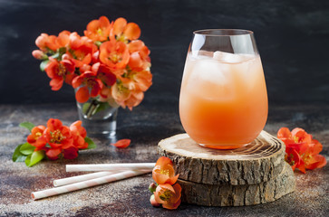 Floral pastel peach and pink brunch cocktail garnished with quince flowers over old rustic...