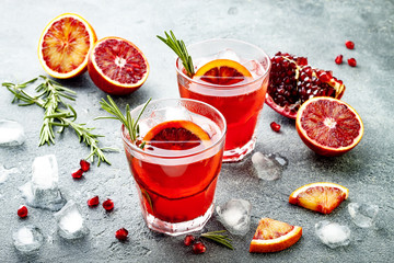 Red cocktail with blood orange and pomegranate. Refreshing summer drink on gray stone or concrete background. Holiday aperitif for Christmas party.