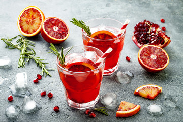 Red cocktail with blood orange and pomegranate. Refreshing summer drink on gray stone or concrete...