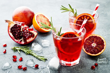 Red cocktail with blood orange and pomegranate. Refreshing summer drink on gray stone or concrete background. Holiday aperitif for Christmas party.