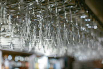Image of wine glasses stacked on black metal hanging bar glass racks in a bar, nightclub or a restaurant with light shining through them.