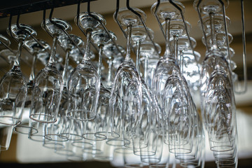 Image of wine glasses stacked on black metal hanging bar glass racks in a bar, nightclub or a restaurant with light shining through them.