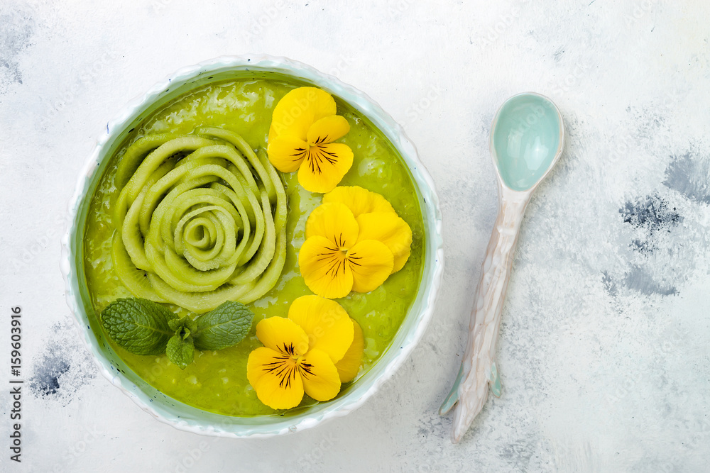 Wall mural Breakfast detox green smoothie bowl topped with kiwi rose and edible Pansy flowers. Overhead, top view, flat lay, copy space