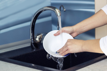 Woman hands rinsing dishes under running water in the sink.