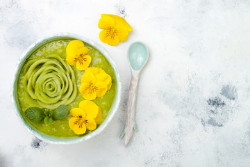 Breakfast detox green smoothie bowl topped with kiwi rose and edible Pansy flowers. Overhead, top view, flat lay, copy space