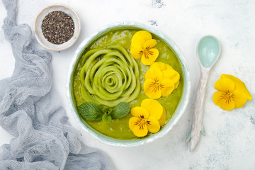 Breakfast detox green smoothie bowl topped with kiwi rose and edible Pansy flowers. Overhead, top view, flat lay, copy space