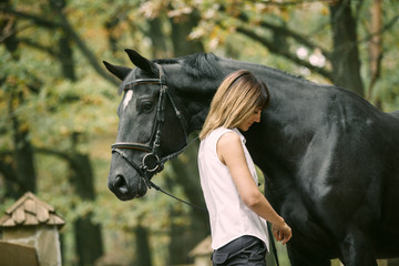 Portrait of young woman and black horse in a forest.
