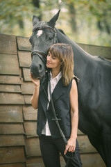 Portrait of young woman and black horse in a forest.