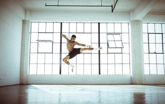 Full length front view of young man in gym in mid air kickboxing stance