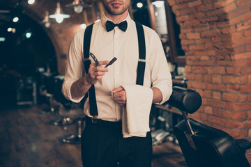 Cropped photo of young guy with bristle in a barber shop, standing with straight razor and towel in his hands, dressed classy in a retro style, ready to do styling