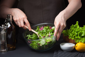 The woman in the process of making vegetable salad. Healthy Eating. Diet Concept. A Healthy Way Of Life. Cook At Home. To Prepare The Food. Girl mixing salad wooden spoon on dark background