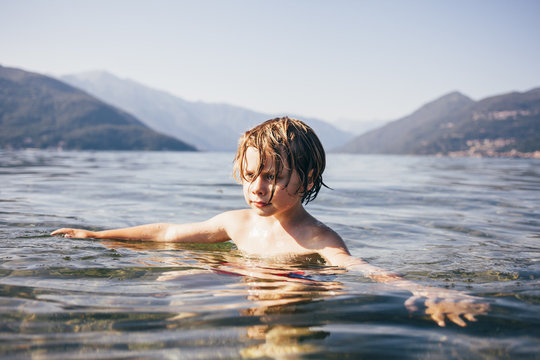 Mountain range and head and shoulders of boy in water arms open looking away, Luino, Lombardy, Italy