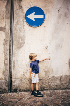 Boy leaning against wall underneath direction sign pointing