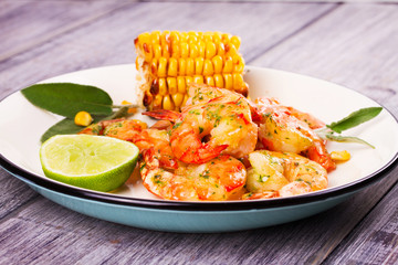 Grilled shrimps and corn garnished with lime and sage leaves. Prawns on white plate