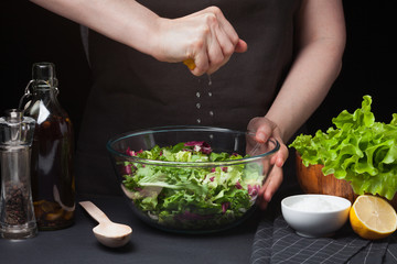 Woman chef in the kitchen preparing vegetable salad. Healthy Eating. Diet Concept. A Healthy Way Of Life. To Cook At Home. For Cooking. Girl squeezes a fresh lemon into a salad on a dark background