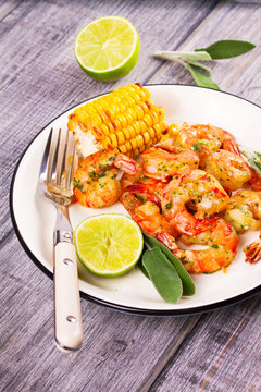 Grilled shrimps and corn garnished with lime and sage leaves. Prawns on white plate