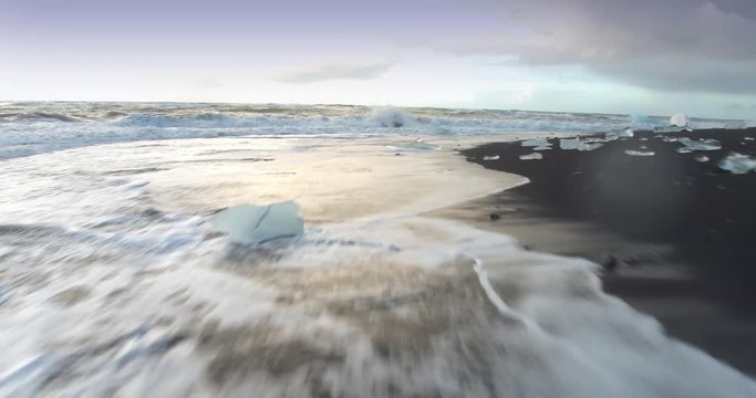 ICELAND &ndash; SEPTEMBER 2016 : Aerial shot over waves washing ashore on diamond beach at sunrise with ice rocks in view
