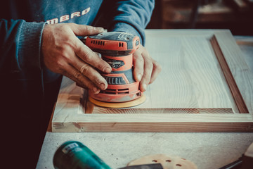 Close-up of carpenter using sander for wood furniture. Soft focus. Shallow DOF.