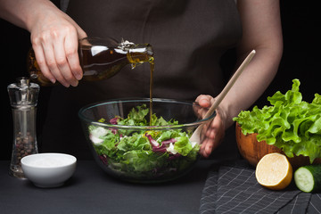 Woman chef in the kitchen preparing vegetable salad. Healthy Eating. Diet Concept. A Healthy Way Of Life. To Cook At Home. The girl behind the salad with olive oil and garlic on a dark background