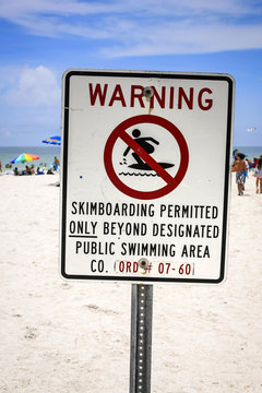 Warning sign about skimboarding in a public swimming area of a Florida beach