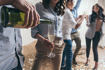 Cropped shot of young man pouring champagne to stylish young woman at party