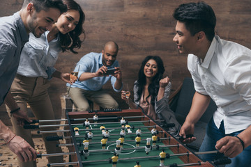 Smiling young friends playing table football together indoors