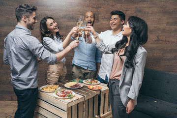 Multiethnic group of cheerful young people clinking champagne glasses above festive table