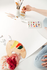 Cropped picture of young lady painter sitting at workspace.