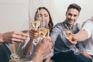 young smiling friends clinking with champagne glasses while sitting at home