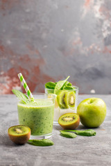 .Green smoothies made of yogurt, spinach, kiwi and apple in glasses on a gray background, ingredients around