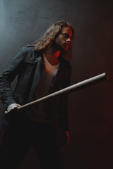 Young long haired man holding baseball bat ready to hit in darkness