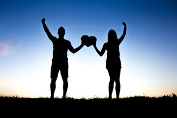 Romantic young couple holding heart shape on hands at sunset