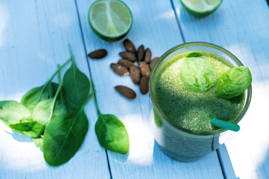 Spinach smoothie on a wooden white background. Glass of smoothie with  leaves of spinach, nuts, limes. Healthy food. Breakfast. Natural light. 