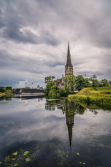 Fototapeta na wymiar Church reflected on water pond in Churchill Park in Copenhagen a cloudy day of summer near sunset.