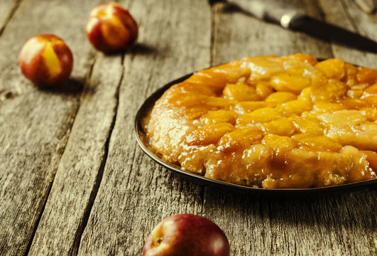 Tarte tatin upside down peach tart on vintage rustic wooden table. Summer baking. French cuisine. Selective focus. Toned image 